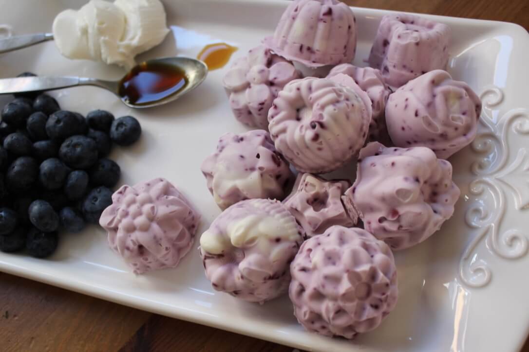 Keto Blueberry Cheesecake Fat Bombs on a white tray with blueberries, cream cheese, and vanilla