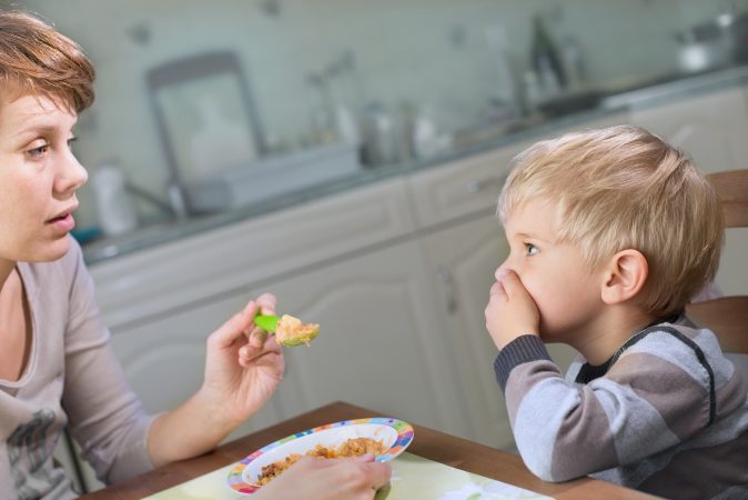 A picky child refuses food from an exasperated mother